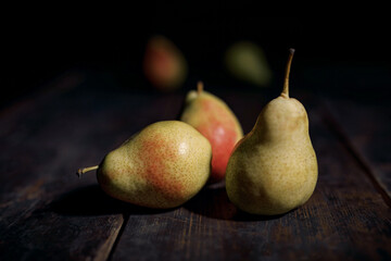 Fototapeta na wymiar three pears on the wooden table and blurred dark background - vintage style photography