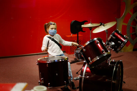 Child In A Mask Plays Drums On A Red Background, A Child Plays A Drum Kit, The Concept Of Musical Development From Early Childhood, Quarantine And Mask Mode