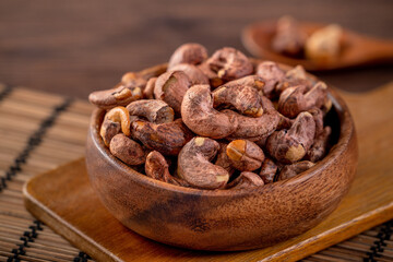 Cashew nuts with peel in a wooden bowl on wooden tray and table background, healthy raw food plate.