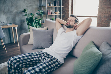 Obraz premium Photo of peaceful quiet man rest relax close eyes sleep stretch hands sit divan wear nightwear sleepwear outfit in apartment house indoors