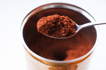 Open package of instant coffee and spoon over white background. Coffee in a metal jar. A spoon over a full can of aromatic coffee. View from above. Selective focus. Close-up