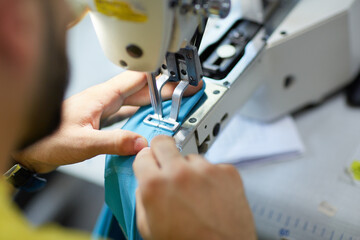 A male worker is working with cover stitch machine in a fabric factory.