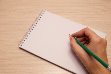 In the right hand of the woman, a green pencil and a white clean notebook for notes