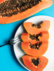 Trozos de papaya con un tenedor en un fondo blanco y azul