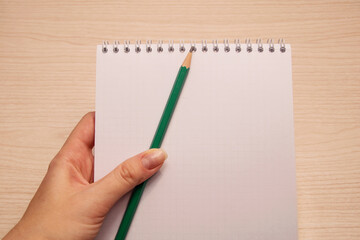 Left female hand holds a green pencil and white clean notebook