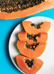 Cuatro trozos de papaya en un plato blanco en un fondo azul