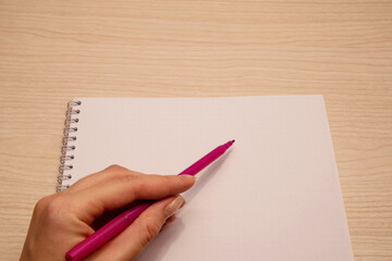 The left hand of the woman holds a purple marker and writes in a clean white notebook.