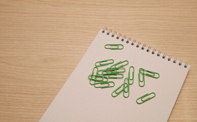 Green paper clips are scattered on a wooden background next to a white clean notebook