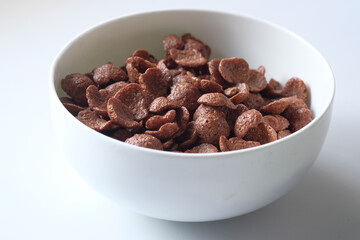 Chocolate breakfast cereal in a white bowl on table.