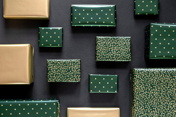 Christmas or New Year gifts in green and gold paper on black background.  Top view.