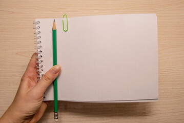 Left female hand holds a white notebook and a pencil on a wooden background