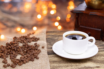A white cup of coffee on a wooden background. A coffee grinder and coffee beens on a linen fabric.Burlap and coffee.