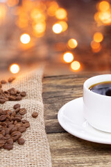 A white cup of coffee on a wooden background. Coffee beens on a linen fabric. Coffee beans on a burlap.