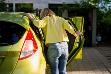 A woman with blonde hair and a yellow sweater gets into a yellow car. A couple of adult people get into a car in front of a modern building.