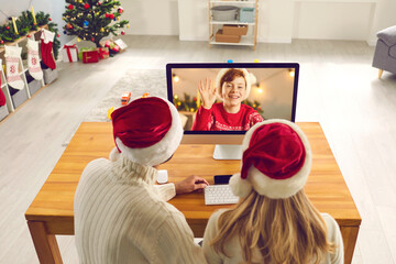 Mom and dad at computer screen video calling their son who's away on Christmas holidays