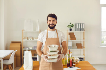Smiling cafe worker in apron uniform holding ready takeaway lunch orders in food containers