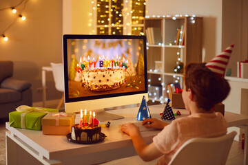 Little boy having online birthday party and looking at beautiful cake on computer screen