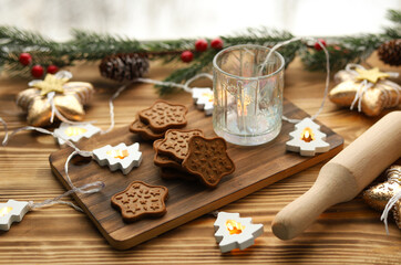 Homemade ginger cookies in the shape of stars on a wooden Board among Christmas lights, a glass candle holder and spruce branches on the windowsill. Cooking holiday sweets.
