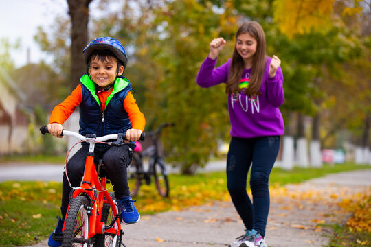 Brother and sister in the park. The boy learns to ride a bike alone. The sister in the background rejoices over his success. Photo on the background of autumn.