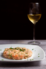 Tapa de tàrtar de salmón con una copa de vino blanco encima de una tabla rústica gris y fondo negro