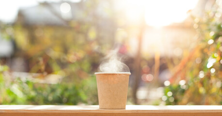 Cardboard cup with hot coffee on the green terrace.
Kartonbecher mit heißem Kaffee auf der grünen Terrasse.