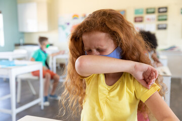 Girl wearing face mask sneezing while covering her mouth at school