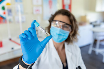 Female teacher wearing face mask and protective glasses holding a test tube with Vaccine text