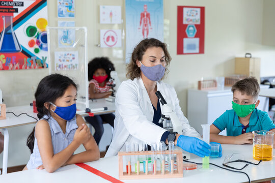Female teacher wearing face mask and protective glasses teaching students in laboratory