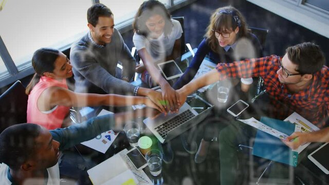 Digital icons against office colleagues stacking hands together