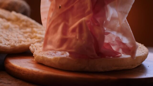 Italian mortadella sandwich on wooden cutting board. Rustic scene describing the filling of bread with sliced mortadella. Dolly and slow motion movement.