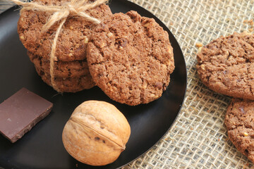 Cookies with chocolate and walnuts on a black plate. Food photo on a natural background made of burlap. Copy space. Clouse up. Top view. Flat lay.
