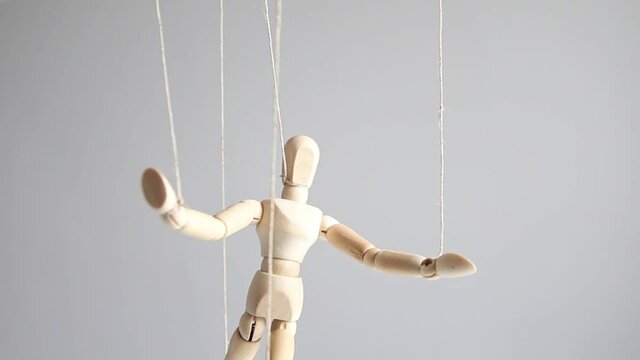 Human wood figure with threads suspended in the air on gray background. Manipulation, addiction concept.
