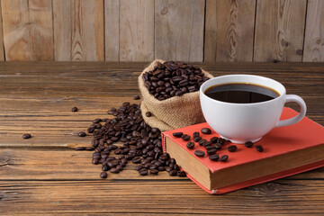 White coffee cup with dark black coffee placed on red books And roasted coffee beans placed on an old wooden table