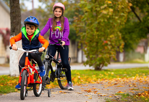 Brother and sister in the park. Boy rides a bike. A girl in the background with a bicycles on a background of autumn. Photo with side space