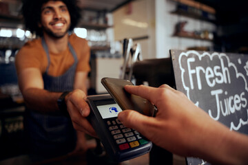 Closeup of young female hand making contactless payment in cafe using smartphone with waiter holding machine - Powered by Adobe