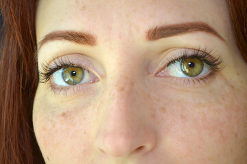 Eyes of woman with red hair and green eyes with freckles with eyelash extension on dark background seriously look forward