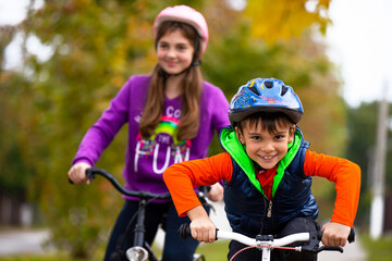 Obraz premium Family holiday. Brother and sister in the park. The boy is alone on the bike. The girl in the background with bicycles on a background of autumn.