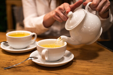 Close up hand pouring tea water from teapot to mug. Defocused background