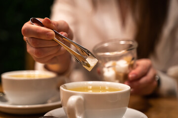 Close-up of a woman's hand throw white sugar into a mug with tea.