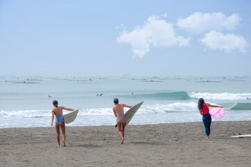 Three surfers walking into water.