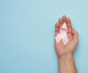 Naklejka premium male hand holds a pink bow-shaped ribbon on a blue background