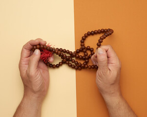two male hands hold wooden prayer beads