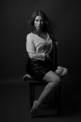 Obraz na płótnie Canvas Low-key black-and-white portrait of a pretty young plus-size model sitting on a chair.