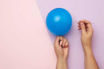 female hand holding a blue balloon and a sharp metal needle