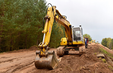 Excavator during construction new road in forest area. Yellow backhoe at groundwork. Earth-moving equipment fort road work, grading, pool excavation, utility trenching. Soft focus, granularity © MaxSafaniuk