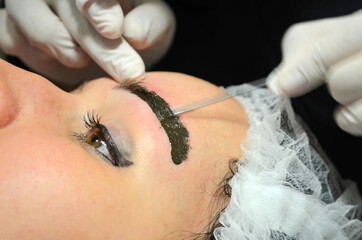 Woman with makeup lying on procedure of microblading. Cosmetologist makes permanent makeup on the...