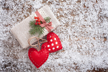 Gift box is festively decorated with hearts and Christmas branch on wooden desk with snow. Selective focus.