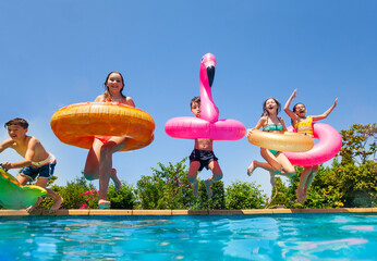 Group of happy little kids dive in water with inflatable toys flamingo doughnut jump into the...