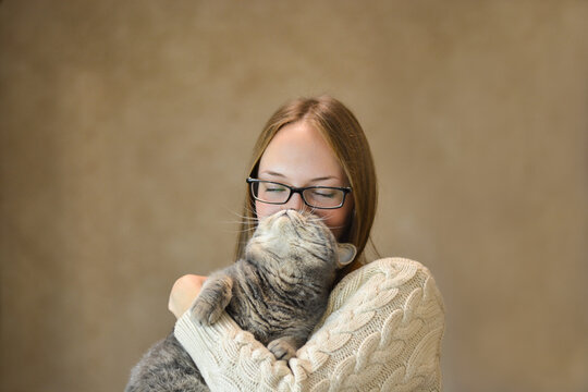 Cute woman with glasses holds a cat near her face.