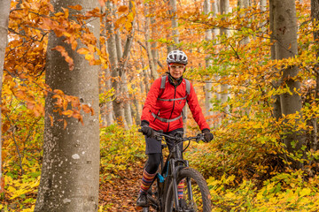 Fototapeta premium sympathetic active senior woman, riding her electric mountainbike in the gold colored autumn forests of the Swabian Alb